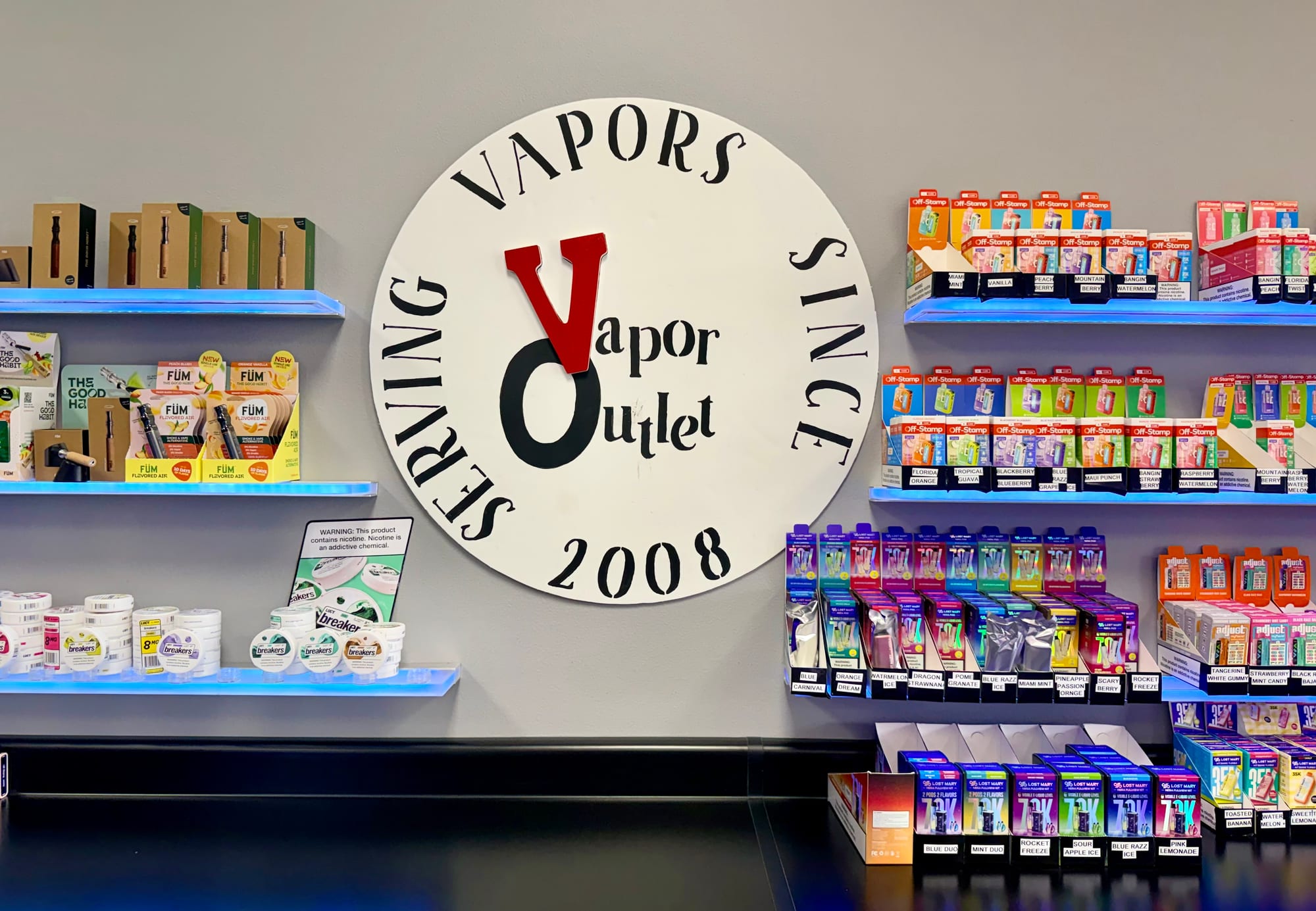 Vapor Outlet — Serving Vapors Since 2008 wall logo, flanked by lit product shelves